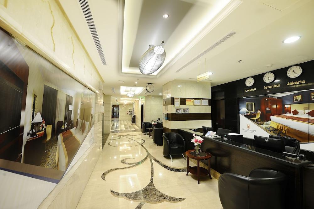 Al Aqeeq Madinah Hotel Medyna Zewnętrze zdjęcie The photo shows the interior of a hotel lobby or reception area. It features a sleek, modern design with elegant marble flooring, decorative lighting fixtures on the ceiling, and a sophisticated color scheme. There are comfortable black seating areas