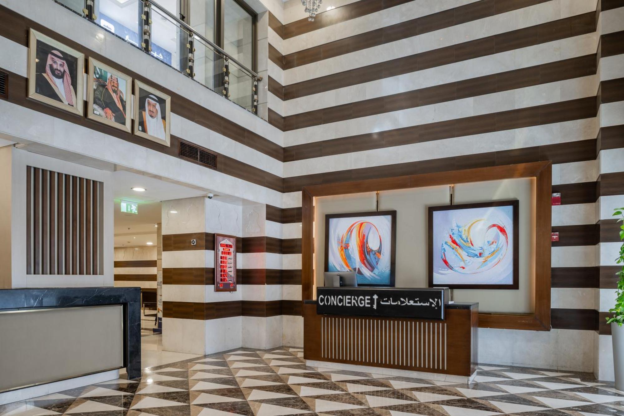 Al Aqeeq Madinah Hotel Medyna Zewnętrze zdjęcie The photo shows a modern hotel lobby area characterized by its stylish design. The walls feature a pattern of horizontal stripes in different shades, creating a sophisticated atmosphere. To the left, there is a reception area with a sleek desk labele