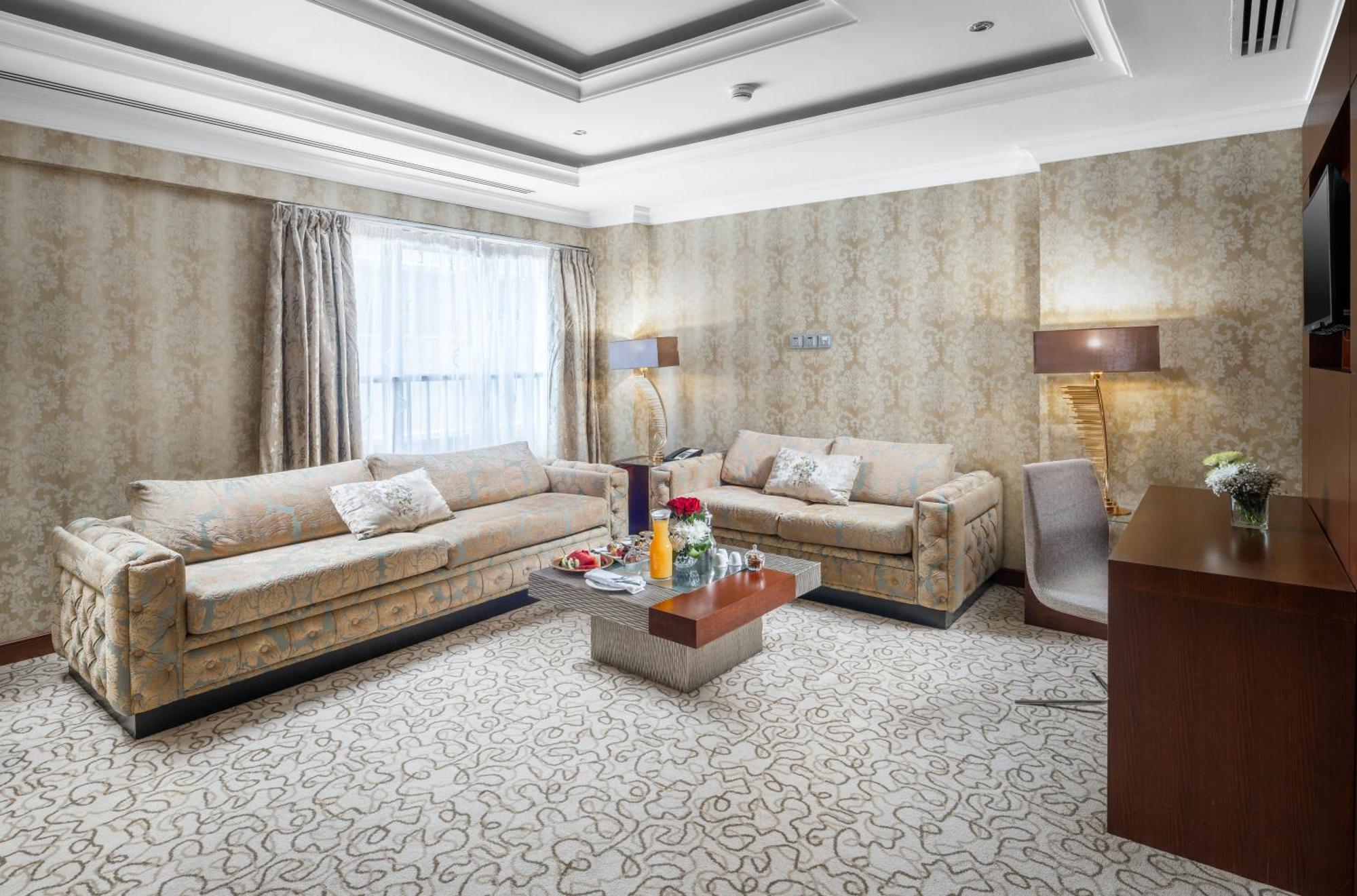 Al Aqeeq Madinah Hotel Medyna Zewnętrze zdjęcie The photo shows a stylish living room with an elegant design. There are two beige sofas placed opposite each other, adorned with decorative pillows. A low coffee table is positioned in the center, featuring various items, possibly drinks or decorativ