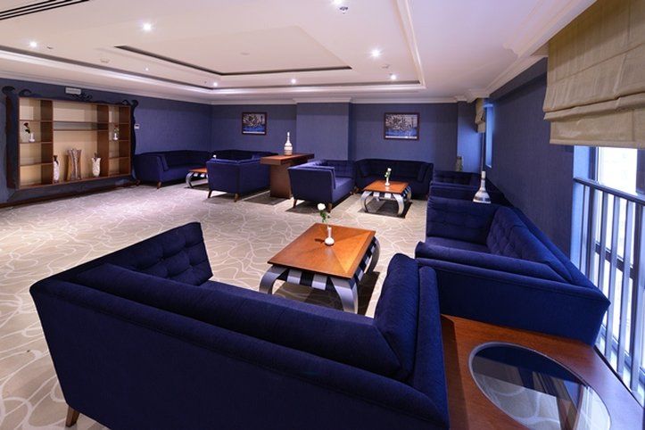 Al Aqeeq Madinah Hotel Medyna Zewnętrze zdjęcie The photo shows a modern lounge area featuring a sophisticated design. The room is painted in a deep blue color, creating a calm and elegant atmosphere. There are several dark blue sofas arranged around a central wooden coffee table. The table is dec